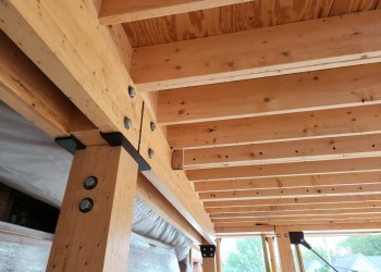 Detail photo of wooden struts and I-beams supporting the second floor of a wooden frame building. The struts are made of multiple boards laminated together to form a strong composite.