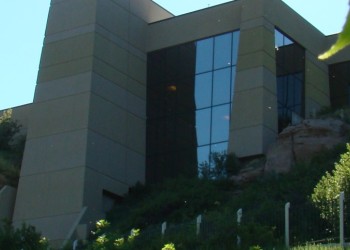 A building with large windows overlooks a steep prairie bluff.