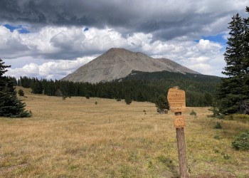 Mountain peak viewed from a distance by a wooden sign.