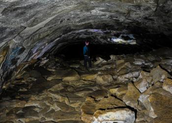 A man stands in the middle of a tube-like cave with a rocky ceiling and rocky floor