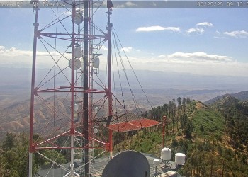 radio tower in front of a green peak over a desert
