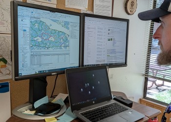 A man sits in front of a set of computer monitors with mapping software on the screen