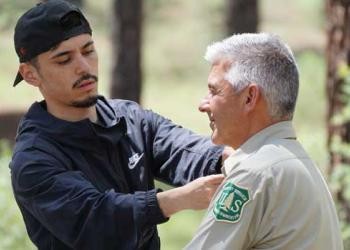 A student filmmaker pins a lapel mic on a Forest Service employee in uniform