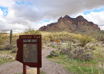 A sign for the Arizona National Scenic Trail before a dirt trail and steep red rocks