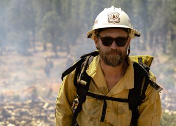 firefighter with helmet, gear, and sunglasses in the forest