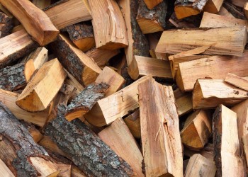 Stacked firewood pieces of various sizes, light brown and tan tones.