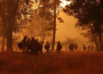 Night crews on Park Fire. Dusk, orange glow in forest with smoke blanketed in the air. Wildland firefighters in gear lined up between tree-lines.