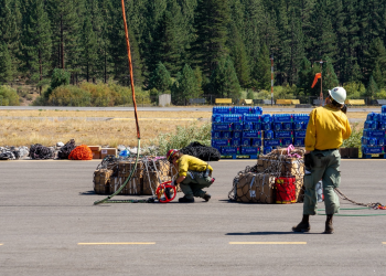 Firefighters hooking supplies to a helicopter with a cord and net during the Park Fire 2024.