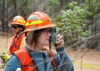 A woman wearing an orange hard hat using a measuring tool.