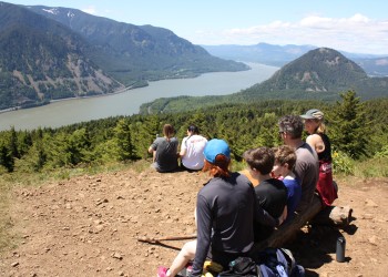 Family of hikers enjoying view from Dog Mountain, sitting on a bench with backs to camera looking out across the gorge.