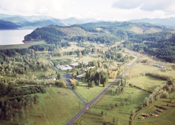 A view from an airplane above a green landscape showing a river in the distance and green hills as well as human structures and roads.