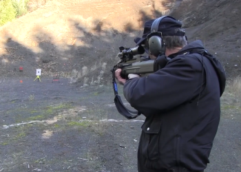 Man with ear protection holding a gun and shooting at a target in a gravel pit.