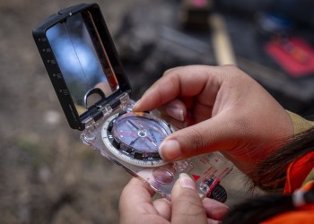 A person adjusts the dial on their compass. View is of their hands holding the compass.