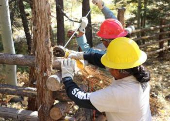 Two students wearing hardhats building a fence.
