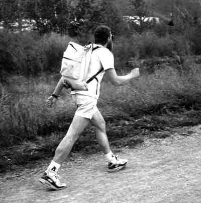 Photo of a man walking briskly with a pack on his back during a work capacity test.