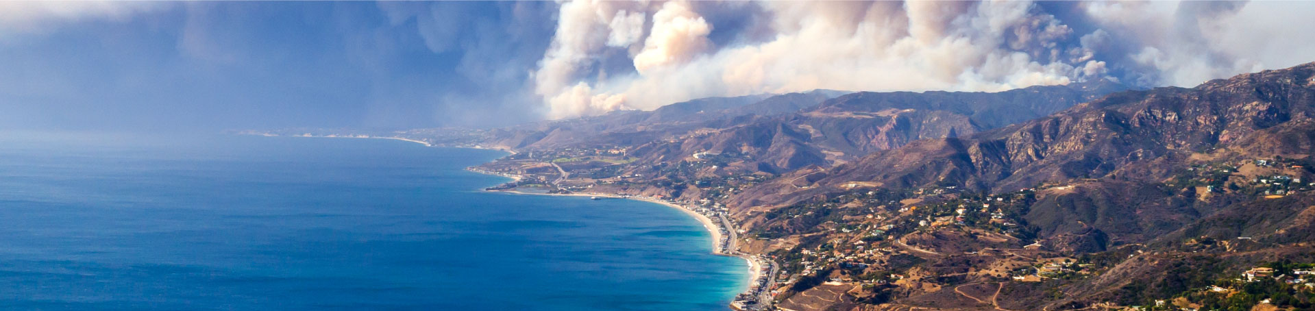 a picture of a beach with the ocean and a wildfire in the background.